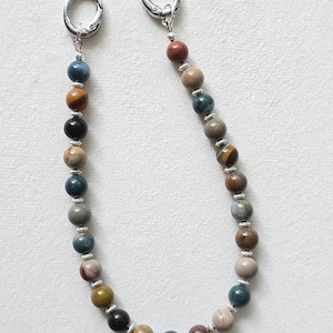 May include: A beaded chain featuring a variety of round, multi-colored natural stone beads in shades of blue, brown, tan, and gray, separated by small silver-toned metal spacers. The chain is finished with two silver-toned metal lobster clasps.