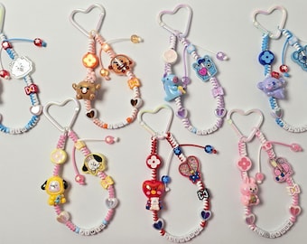 May include: Seven beaded lanyards featuring heart-shaped clasps, colorful plastic beads, and various character charms. Each lanyard includes letter beads spelling out names like JIN, SUGA, J-HOPE, RM, JIMIN, V, and JUNGKOOK in a mix of pastel and vibrant tones.