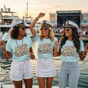 Könnte beinhalten: Drei hellblaue T-Shirts mit dem Schriftzug Yacht Rock Flock und einer bunten Grafik aus Flamingos und Regenbögen. Jedes Shirt wird mit einer weißen Kapitänsmütze mit goldenen Verzierungen kombiniert, getragen auf einem Bootsdeck.