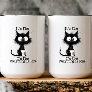 May include: Two white ceramic mugs with black rims and handles. Each mug features a black cat illustration with the text "It's Fine, I'm Fine, Everything is Fine". The cat is holding a small cup.