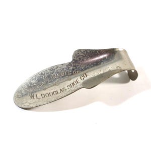 May include: A silver metal shoe horn with the text "COMPLIMENTS OF W.L.DOUGLAS SHOE CO." engraved on the surface.