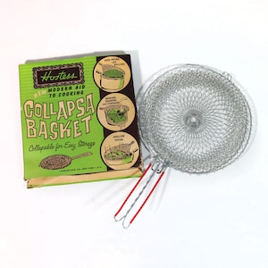 May include: A vintage Hostess Collapsa Basket for cooking, washing, draining, and shallow frying. The collapsible basket is made of silver wire mesh with red and silver handles. The green and white box features illustrations and text.