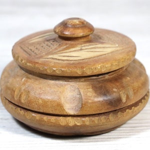 May include: A small, round wooden box with a lid. The box is carved with a simple design and has a light brown color.