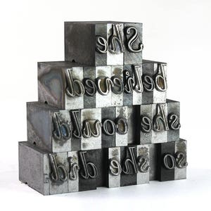 May include: A stack of metal letterpress blocks spelling out the phrase "She believed she could so she did".