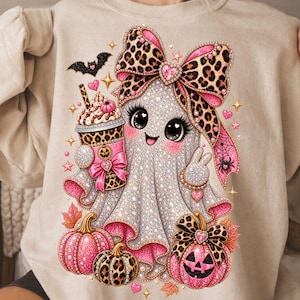 Peut inclure: Un sweat-shirt beige à col rond orné d'un motif représentant un fantôme blanc pailleté avec un grand nœud à imprimé léopard, tenant une tasse à café rose à imprimé léopard. Le design inclut des citrouilles roses, une chauve-souris noire et des étoiles.