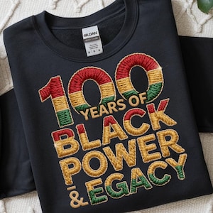Könnte beinhalten: Schwarzes Sweatshirt mit gesticktem Text "100 YEARS OF BLACK POWER & LEGACY". Die Zahlen und Buchstaben sind rot, gold, grün und gelb. Das Sweatshirt hat einen Rundhalsausschnitt und lange Ärmel. Das Markenetikett ist sichtbar.