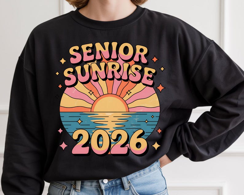 May include: Black sweatshirt featuring a retro design with the words "SENIOR SUNRISE 2026" in pink and orange. The graphic includes a stylized sunset over water with a color palette of orange, pink, and blue. Small star shapes surround the design.