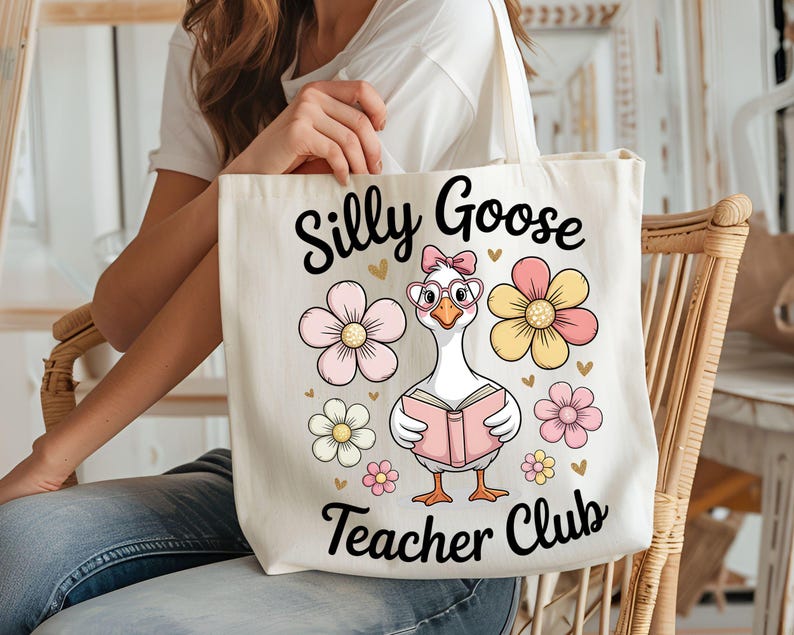 Może przedstawiać: Kremowa torba z napisem "Silly Goose Teacher Club". Torba przedstawia kresk&oacute;wkową gęś w okularach i kokardzie, trzymającą książkę, otoczoną r&oacute;żowymi i ż&oacute;łtymi kwiatami. Zabawny i fantazyjny design.