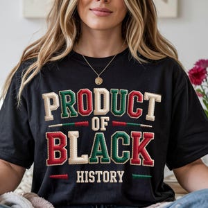 May include: Black t-shirt with the text "PRODUCT OF BLACK HISTORY" in a bold, stitched design. The text features green, red, and cream colours. The shirt is a casual wear item, suitable for everyday use.