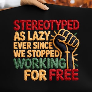 May include: Black tote bag with the embroidered text "STEREOTYPED AS LAZY EVER SINCE WE STOPPED WORKING FOR FREE" in red, yellow, and green. A raised fist graphic is also embroidered in black and yellow.