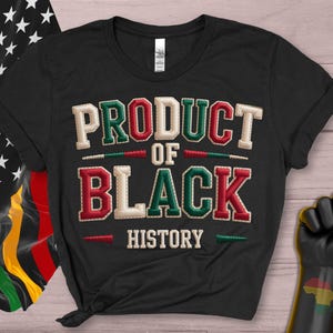 May include: Black t-shirt featuring the text "PRODUCT OF BLACK HISTORY" in green, red, and white stitched lettering. The image includes a Black Power fist and a flag with stars and the Pan-African colours.