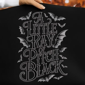 May include: Black rectangular item featuring the phrase "A Little Ray of Pitch Black" in a gothic font, with bat illustrations. The bats and text are light grey.