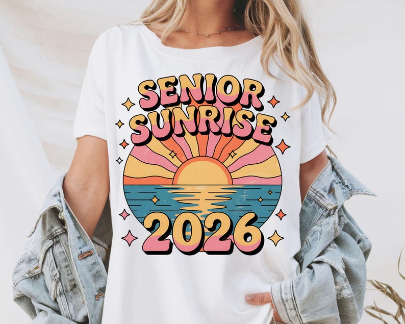 May include: White t-shirt featuring a retro design with the words "SENIOR SUNRISE" in a layered, colorful font. Below the text is a sunset scene over water, with the year "2026" in a matching font. The design includes star accents.