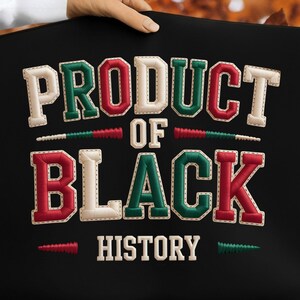 May include: Black fabric with the embroidered text "PRODUCT OF BLACK HISTORY" in white, red, and green. The letters have a stitched outline. The words are arranged in two lines with decorative elements.