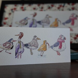 Può includere: Illustrazione ad acquerello di sei uccelli stravaganti, ognuno adornato con abiti unici come sciarpe e cappelli. Gli uccelli sono raffigurati su una carta bianca, con una stampa incorniciata di uccelli simili sullo sfondo. L'opera d'arte ha uno stile affascinante e artistico.