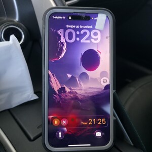 May include: A smartphone in a dark grey protective case displaying a lock screen with a purple space-themed wallpaper. The screen shows the time 10:29, a T-Mobile signal indicator, and an active timer counting down from 21:25 with pause and cancel icons.