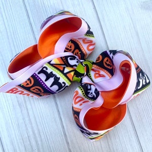 May include: A large pink and orange bow with a Halloween print. The print features black cats, pumpkins, candy corn, and the words "Boo!" and "Boo-tiful!"