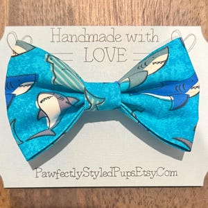 May include: A blue bow tie with a shark pattern. The bow tie is handmade with love and is available on Etsy.