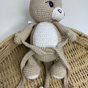 May include: A handmade crochet kangaroo doll in beige and white. The kangaroo has a white belly, black eyes, and a small black nose. The doll is sitting in a woven basket.