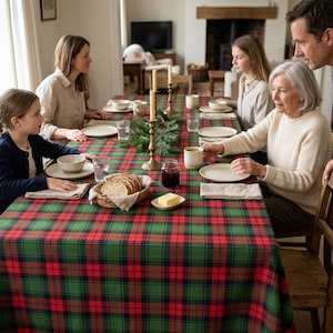 May include: A rectangular tablecloth featuring a classic red, green, and black plaid pattern. The fabric covers a long dining table set with ceramic plates, bowls, glasses, a bread basket, a butter dish, and two tall brass candlesticks.