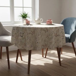 Puede incluir: Una mesa redonda cubierta con un mantel floral. Dos rebanadas de pastel con bayas rojas est&aacute;n en platos. Tambi&eacute;n hay una tetera blanca y dos sillas. La mesa tiene patas de madera.
