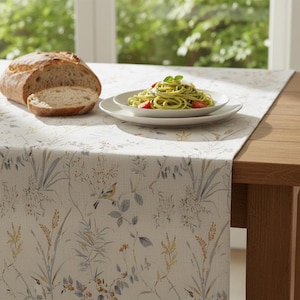 Puede incluir: Una mesa puesta con pan, un plato de pasta con pesto y tomates, y un camino de mesa con estampado floral. El camino de mesa tiene un fondo crema con ilustraciones bot&aacute;nicas en tonos apagados.