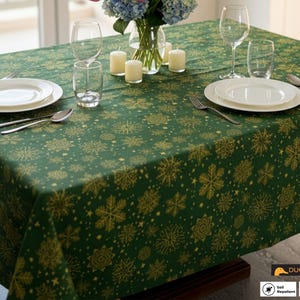 Op de afbeelding: Een groene tafelkleed met een gouden sneeuwvlokpatroon, gedekt voor een formeel diner. De tafel is gedekt met witte borden, bestek, wijnglazen en kaarsen. Het tafelkleed is vuil- en waterafstotend.