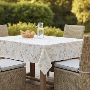 Puede incluir: Un juego de mesa de comedor al aire libre con un mantel floral. Sillas de mimbre con cojines grises rodean la mesa. Una cesta de panecillos y una jarra de agua con rodajas de lim&oacute;n est&aacute;n sobre la mesa.