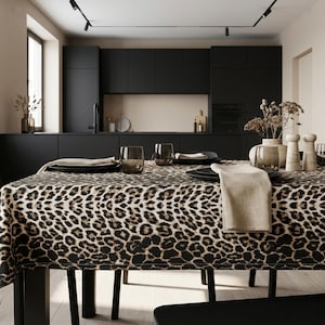 Könnte beinhalten: Ein Esstisch mit einer Tischdecke mit Leopardenmuster. Der Tisch ist mit schwarzen Tellern, klaren Gläsern und einer beigen Leinen-Serviette gedeckt. Der Raum hat schwarze Schränke und ein neutrales Farbschema.
