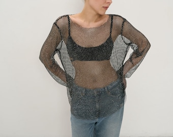 May include: A black mesh long-sleeve top with a round neckline. The top is worn over a black bra and paired with light blue denim jeans with distressed details. The outfit is set against a plain white background.