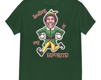 May include: A dark green t-shirt with a cartoon illustration of an elf character. The character is smiling and running, with the words "Smiling is my favorite!" in red and white text.