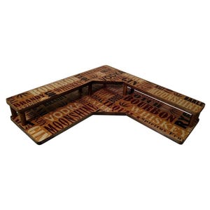 May include: A wooden, L-shaped bar with a brown finish. The surface is covered with words like "Bourbon," "Whiskey," and "Vodka." The bar has a raised edge and is designed for serving drinks.