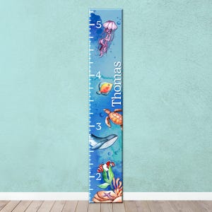 May include: A blue growth chart featuring watercolor illustrations of marine life, including a jellyfish, fish, turtle, whale, and clownfish. The chart is marked with numbers and the name "Thomas".