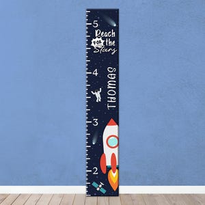 May include: A dark blue growth chart with a space theme. It features a rocket, astronaut, and the text "Reach for the Stars" and "Thomas". The chart measures up to 5 feet.