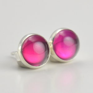 May include: A pair of silver stud earrings with round, pink gemstones.