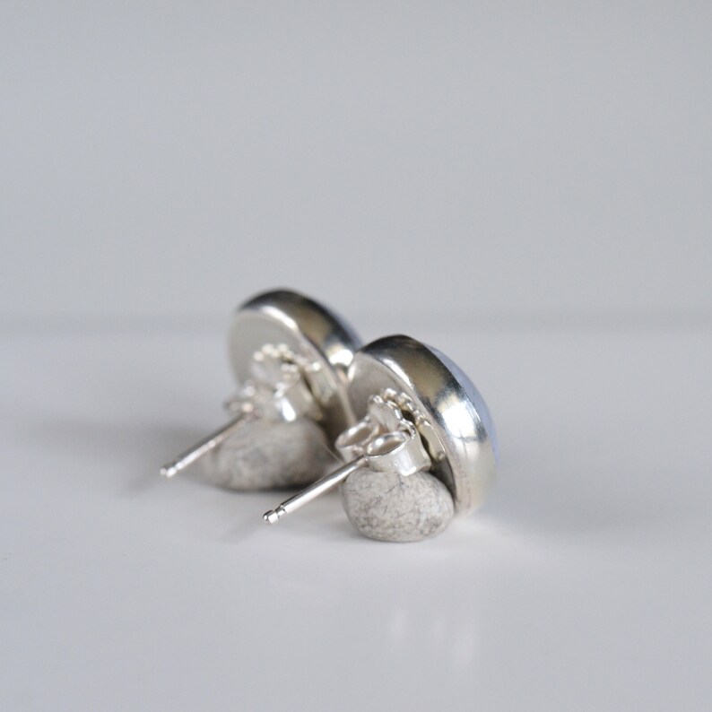 May include: A pair of silver stud earrings with light blue round stones. The earrings are shown from the back, with the post and butterfly backing visible.