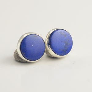 May include: A white ceramic mug with a black handle and the text "But First, Coffee" in a bold, black font. The mug is set against a blurred background, suggesting a cosy setting.