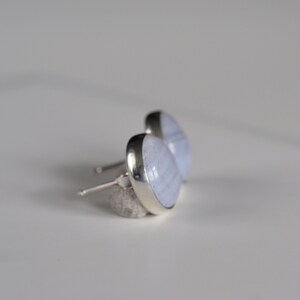 May include: A pair of silver stud earrings with light blue agate stones. The stones have a white and light blue banded pattern.