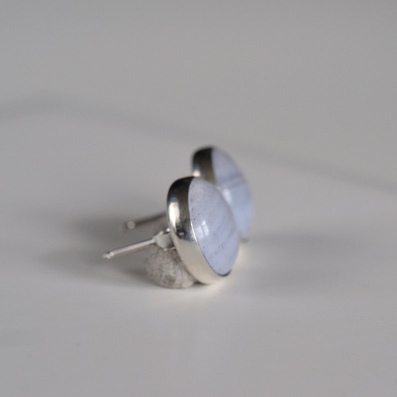 May include: A pair of silver stud earrings with light blue agate stones. The stones have a white and light blue banded pattern.