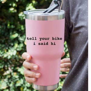 Peut inclure: Un gobelet isotherme en acier inoxydable rose avec un couvercle et une paille noirs. Le gobelet porte l'inscription "tell your bike i said hi".