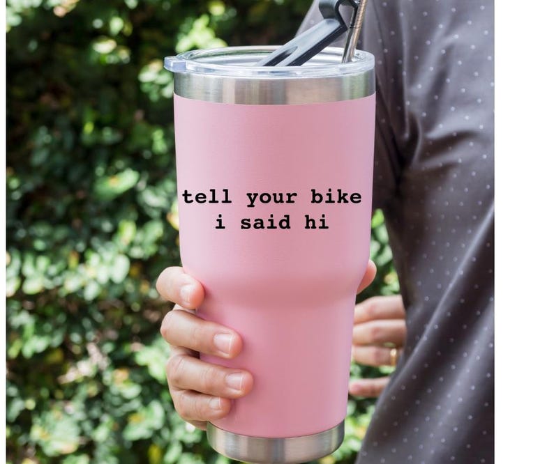 Peut inclure: Un gobelet isotherme en acier inoxydable rose avec un couvercle et une paille noirs. Le gobelet porte l'inscription "tell your bike i said hi".