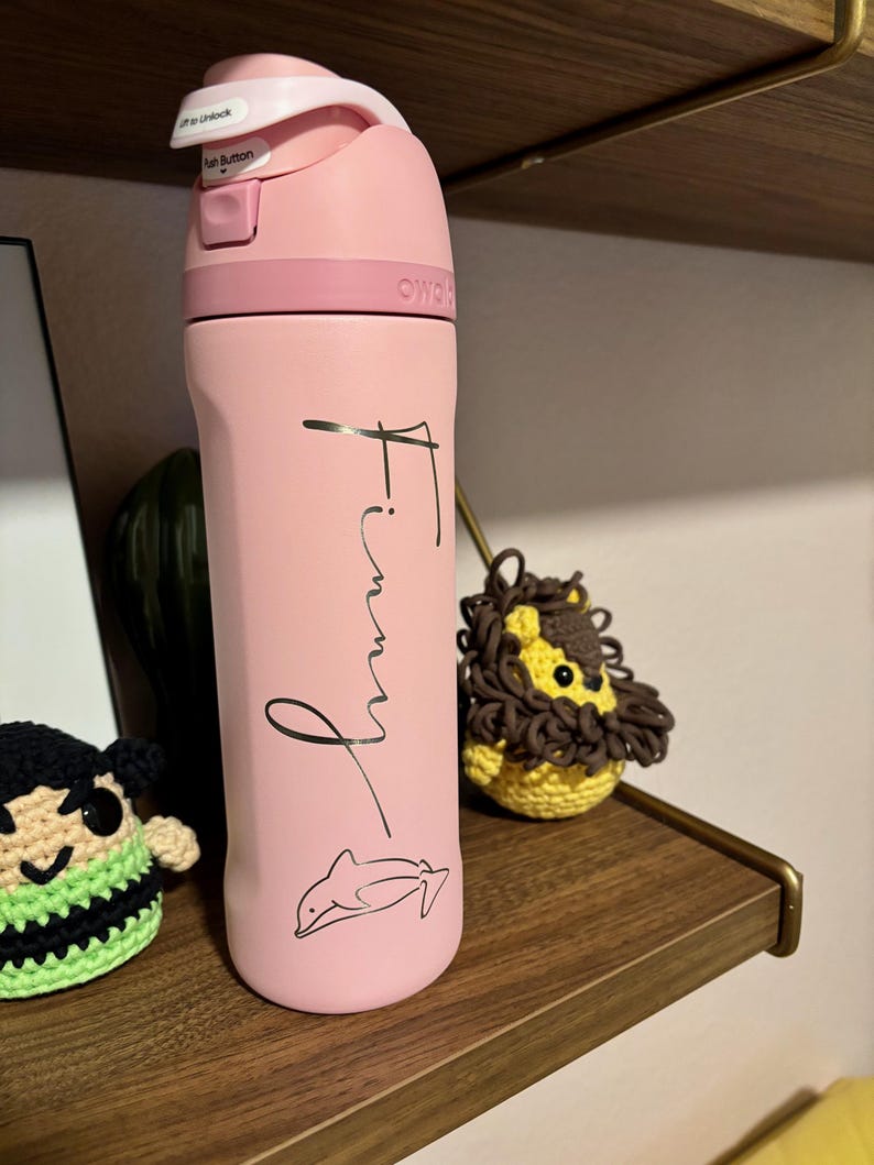 May include: Pink water bottle with a black dolphin design and the name "Finny" written in cursive on the side.