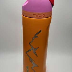 May include: Orange stainless steel water bottle with a pink lid and a mountain design. The bottle has the word "owala" printed on it.