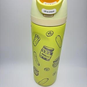 May include: A yellow stainless steel water bottle with a green lid and a yellow top. The bottle has a print of pickles and pickle jars on it. The lid has the text "Lift to Unlock".
