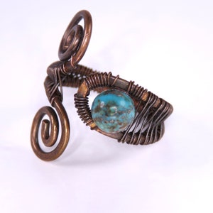 May include: A copper wire ring with a turquoise gemstone. The ring is made of wire that is twisted into a spiral shape. The gemstone is set in a wire cage.