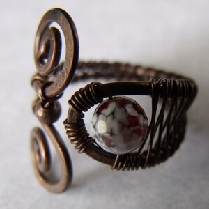 Op de afbeelding: Een koperen draadring met een swirl-ontwerp en een rood-witte agaat-steen.