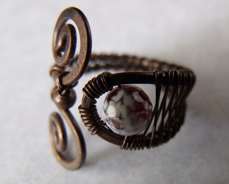 Op de afbeelding: Een koperen draadring met een swirl-ontwerp en een rood-witte agaat-steen.