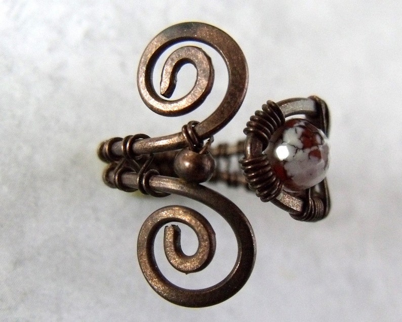 Op de afbeelding: Een ring van koperdraad met een witte en bruine agaat steen. De ring is gemaakt met twee draadspiralen aan weerszijden van de steen.