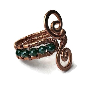 May include: A copper wire ring with a green gemstone design. The ring features two copper wire spirals and a row of green gemstones.