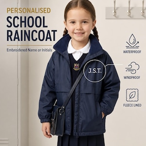 May include: A navy blue school raincoat featuring a high collar, long sleeves with elastic cuffs, and a front zip. The jacket displays the embroidered initials J.S.T. on the chest. Text on the image includes PERSONALISED SCHOOL RAINCOAT, Embroidered Name or Initials, WATERPROOF, WINDPROOF, and FLEECE LINED.
